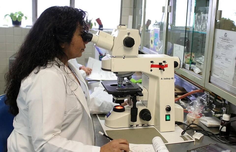 Uma pesquisadora observando algo em um microscópio.
