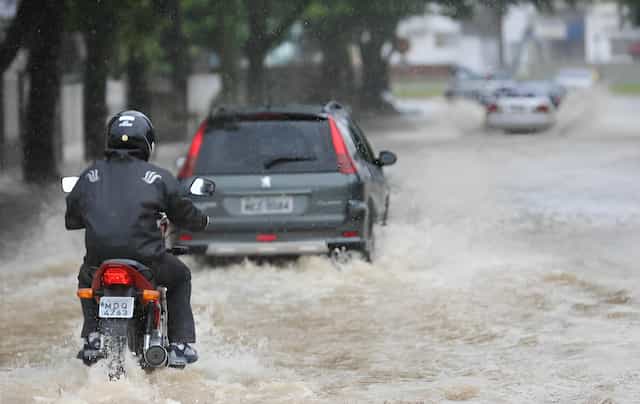 Uma moto e um carro passando por uma enchente.